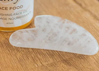 White quartz gua sha stone next to a Mushroom Envy Face Food oil bottle on a wooden table