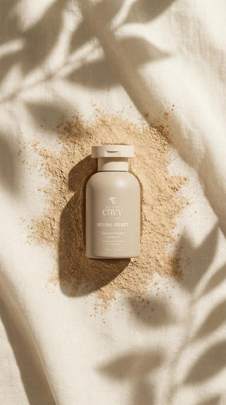 Reishi Reset gentle powder cleanser bottle lying on a scatter of its own powder on cream linen with leaf shadows