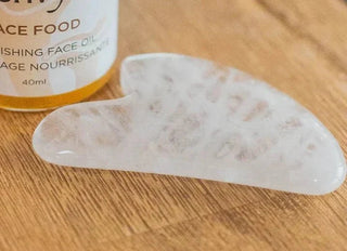 White quartz gua sha stone next to a Mushroom Envy Face Food oil bottle on a wooden table