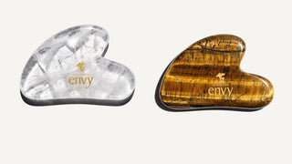 White quartz and tiger eye gua sha stones with the Mushroom Envy logo, side by side on a light background